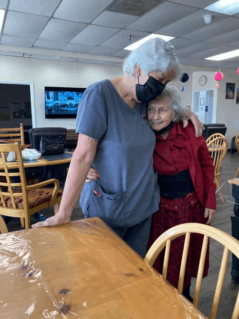 a woman wearing a mask hugs an older woman