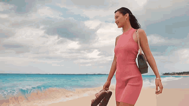 a woman in a pink dress walks along the beach