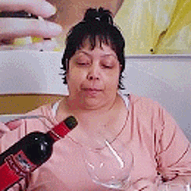 a woman is sitting at a table holding a bottle of wine and a glass of wine .