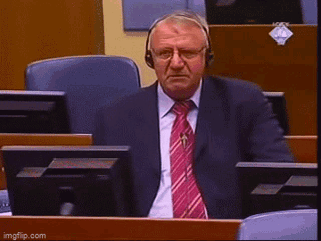 a man in a suit and tie is sitting in front of a computer with the words i ne volim vas written below him