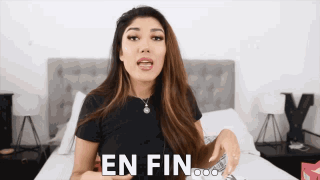 a woman in a black shirt is sitting on a bed with the words " en fin " on the bottom