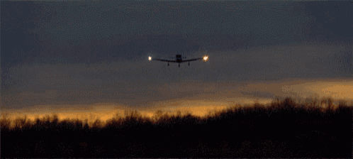 a plane is taking off from a runway at night with a sunset in the background