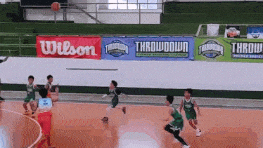 a group of young boys are playing a game of basketball on a court with a wilson banner in the background .
