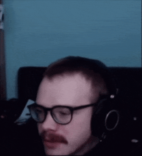 a man with glasses and a mustache is wearing headphones and making a funny face .