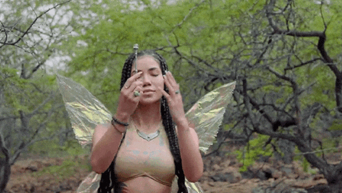 a woman dressed as a fairy with wings is covering her eyes in the woods .