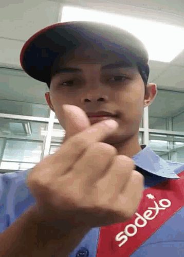 a man wearing a sodexo shirt is making a heart shape with his finger