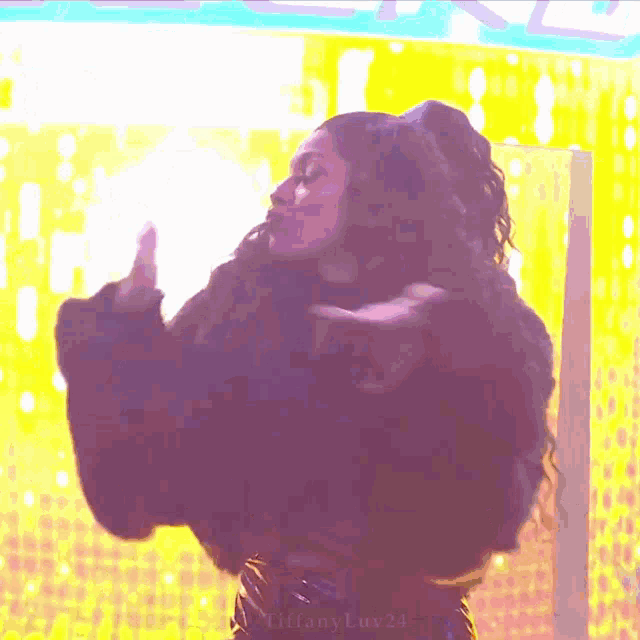 a woman is standing in front of a yellow wall giving the middle finger .