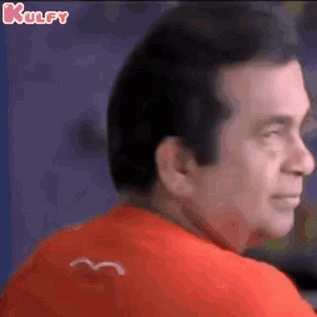a man wearing a red shirt with a bird on the back is looking over his shoulder .