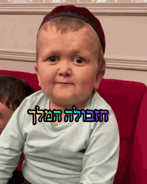 a baby is sitting on a red couch with a sticker that says ' hebrew ' on it