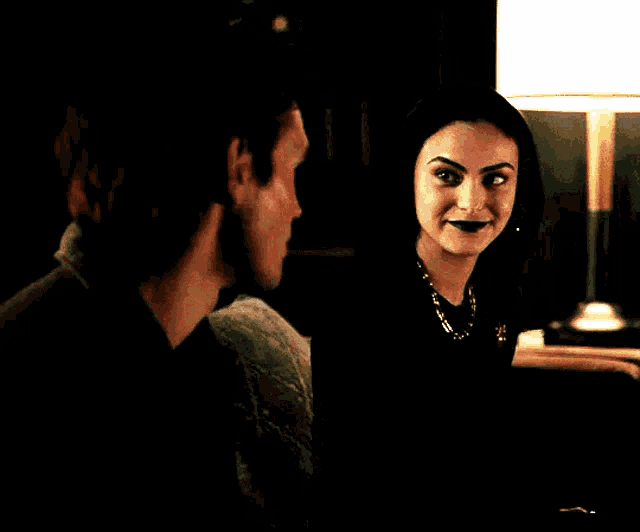 a man and a woman are looking at each other in a dark room with a lamp in the background .
