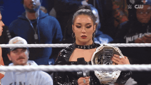 a woman in a wrestling ring holds a championship belt and a microphone
