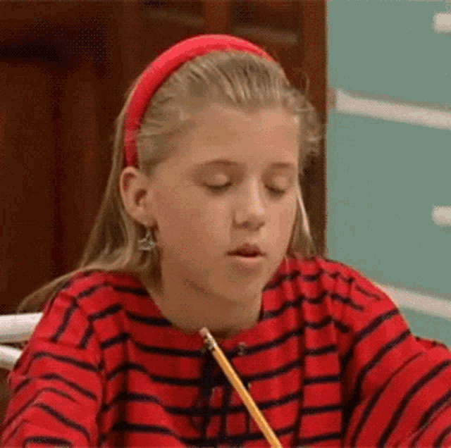 a young girl wearing a red headband is sitting at a desk with a pencil .