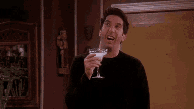a man in a black shirt is holding a martini glass and making a surprised face .