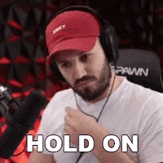a man wearing headphones and a red hat says hold on .