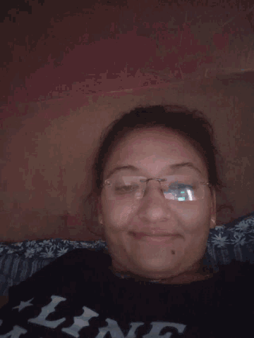 a woman wearing glasses is laying on a bed with a shirt that says ' pink ' on it
