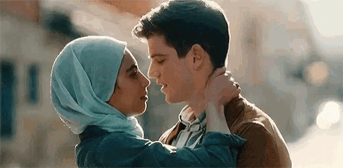 a man and a woman are kissing each other on the forehead . the woman is wearing a hijab .