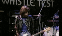 a man in a leather jacket is playing a guitar in front of a sign that says whistle test