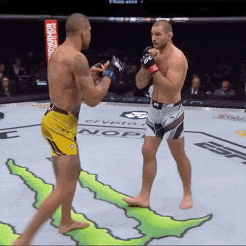 two men are fighting in a boxing ring with a monster energy logo on the floor