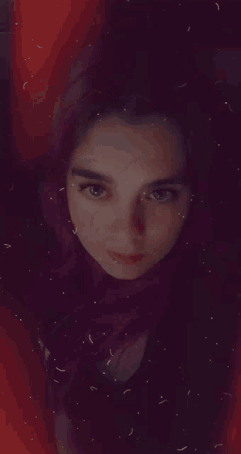 a woman with purple hair looks at the camera with a red background
