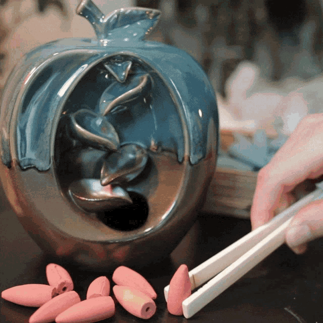 a person is holding a pair of chopsticks in front of a ceramic apple shaped burner
