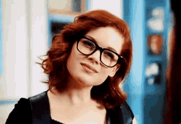 a woman with red hair and glasses is smiling for the camera