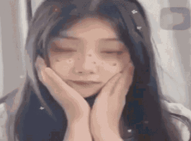 a girl with long black hair is smiling with her hands on her face .