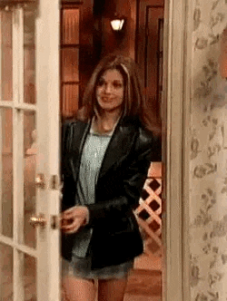 a woman is standing in a doorway wearing a leather jacket and shorts .