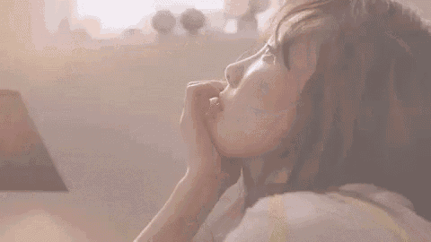 a woman is laying in bed with her hand on her chin and looking out the window .