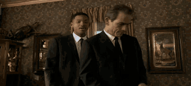 two men in suits and ties are standing in a room