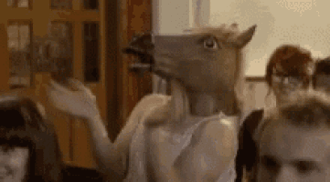 a woman wearing a horse head mask is standing in front of a crowd of people .