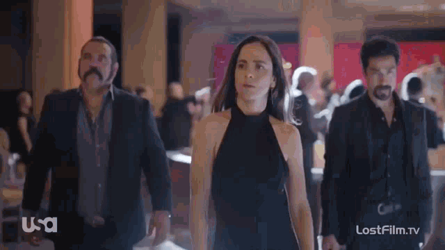 a woman in a black dress is walking with two men in suits with usa written on the bottom right