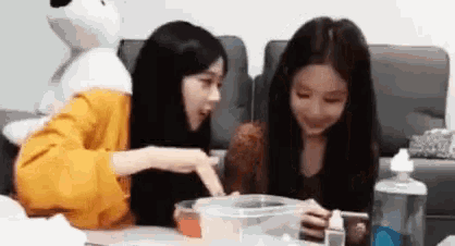 a couple of girls are sitting at a table looking at a cell phone .
