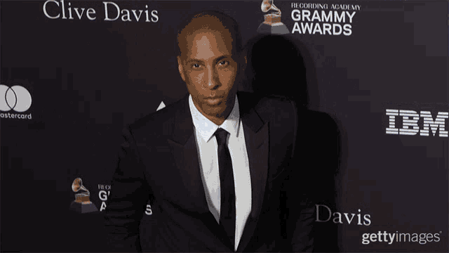 a man in a suit and tie stands in front of a recording academy grammy awards poster