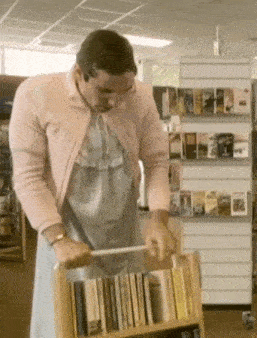 a man in a pink cardigan is pushing a cart of books