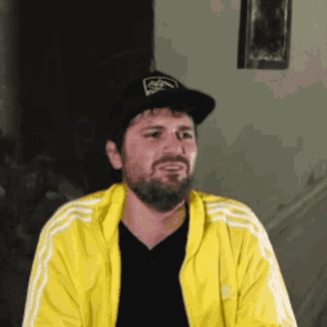 a man with a beard wearing a yellow adidas jacket and a black hat