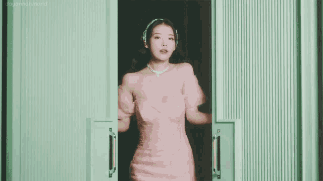 a woman in a pink dress is standing in front of a green wall