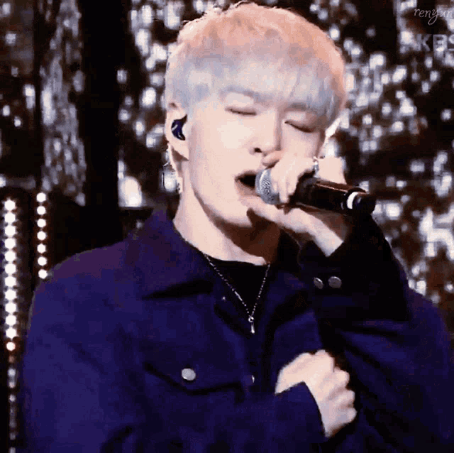 a young man is singing into a microphone while wearing a blue jacket