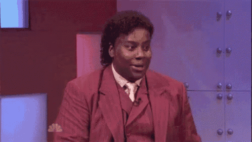 a man in a red suit and tie is sitting on a stage with his mouth open and a surprised look on his face .