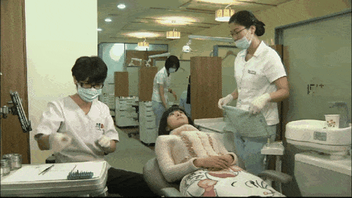 a woman in a dental chair is being examined by two dentists and a nurse