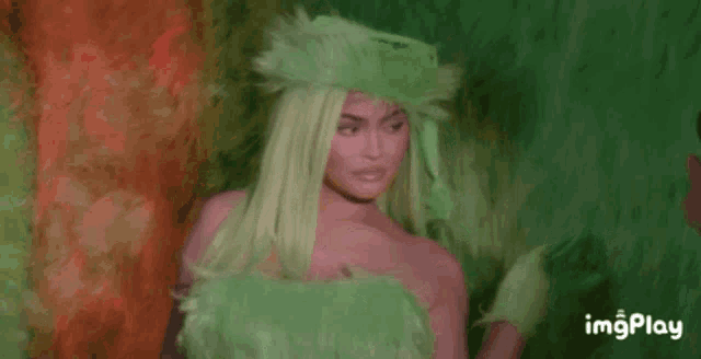 a woman in a green wig and green gloves is standing in front of a green background .