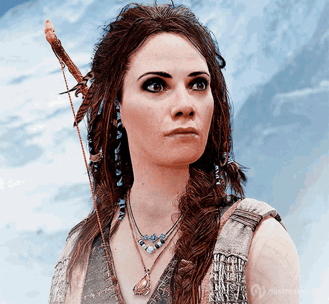 a woman with feathers in her hair holds a spear in her right hand