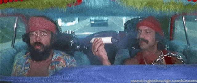 two men are sitting in a car looking out the window and one is holding a bottle .