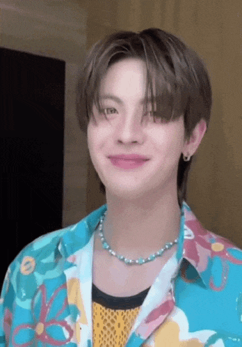 a young man wearing a floral shirt and a blue necklace is smiling .
