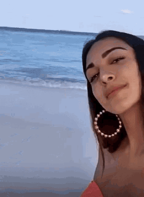 a woman wearing hoop earrings is standing on the beach looking at the ocean .