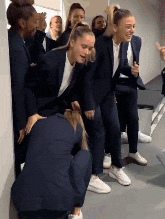 a group of women wearing suits and white sneakers are dancing