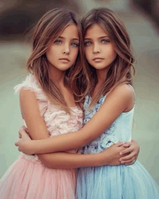 two young girls are hugging each other while wearing dresses .