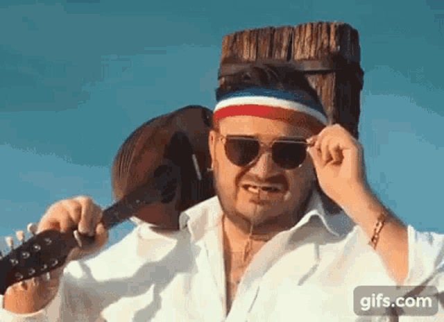 a man wearing sunglasses and a headband is holding a guitar and a mandolin .