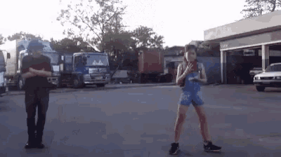 a man and a woman are standing in a parking lot with trucks in the background .