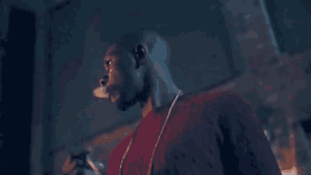 a man in a red shirt is smoking a cigarette with smoke coming out of his mouth