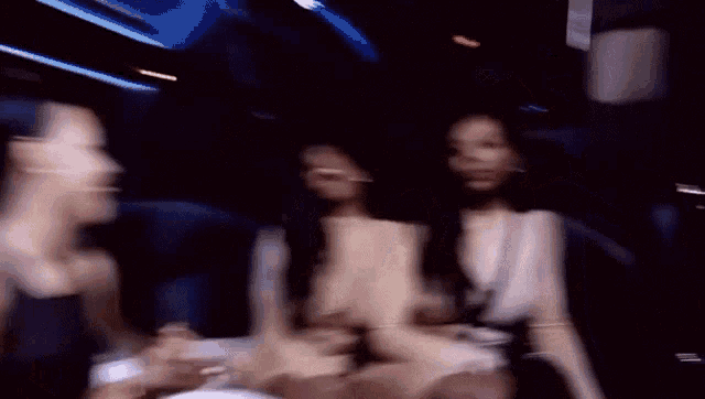 two women in tight dresses are sitting in a limo and raising their hands in the air .